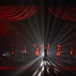 A group of dancers on stage in front of a red curtain.
